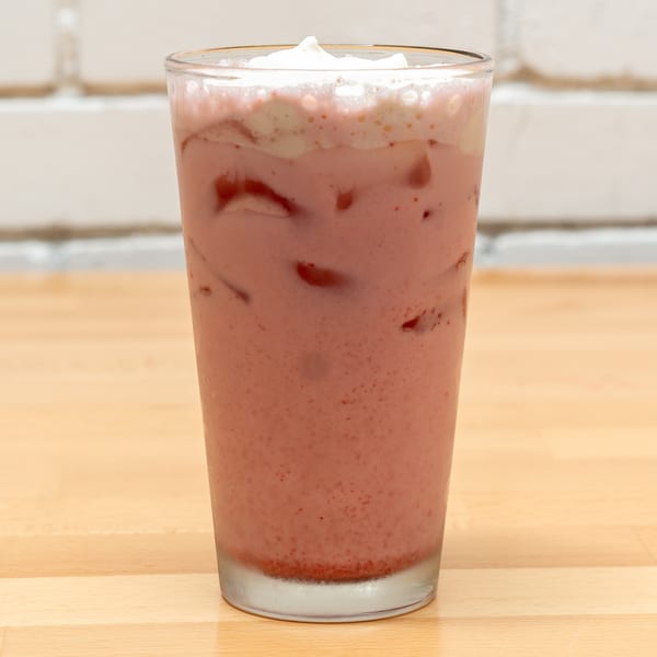 A tall glass of pink strawberry milkshake with whipped cream on a wooden table.