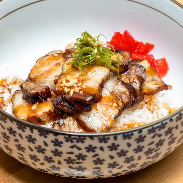 Japanese chashu pork slices over white rice, garnished with green onions and red pickled ginger.