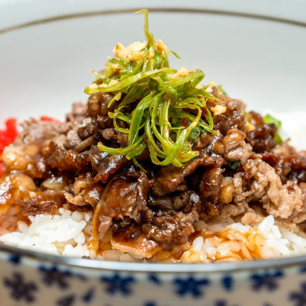 Close-up of a Japanese beef bowl with rice, topped with green onions and red ginger.