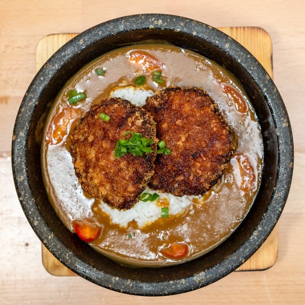 Japanese curry with two crispy fried cutlets, rice, and chopped scallions in a dark bowl.