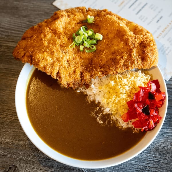 A large plate of Japanese curry with a golden-brown fried cutlet, rice, and red pickled vegetables.