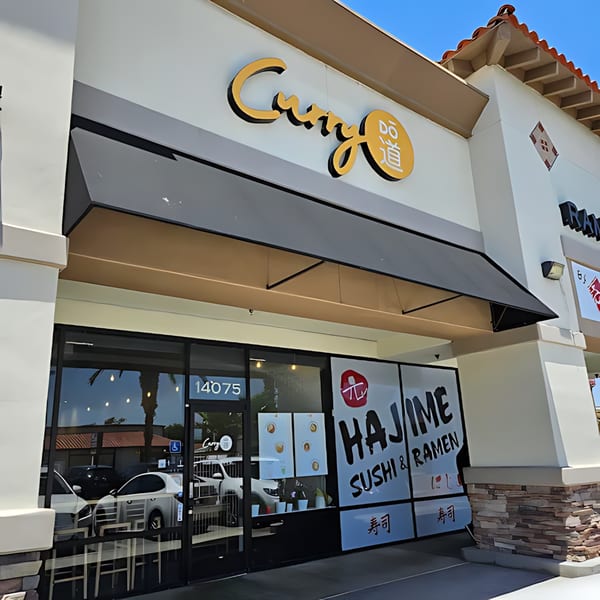 Exterior of Curry Do Japanese restaurant with a black awning and large glass windows.