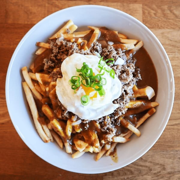 Japanese curry poutine with fries, gravy, ground beef, a fried egg, and green onions.
