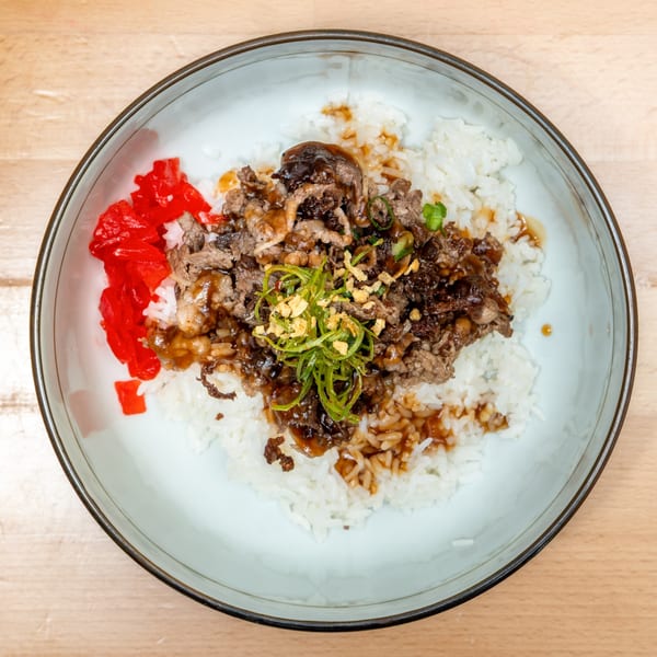 Japanese Gyudon bowl with beef, rice, green onions, and red pickled ginger.