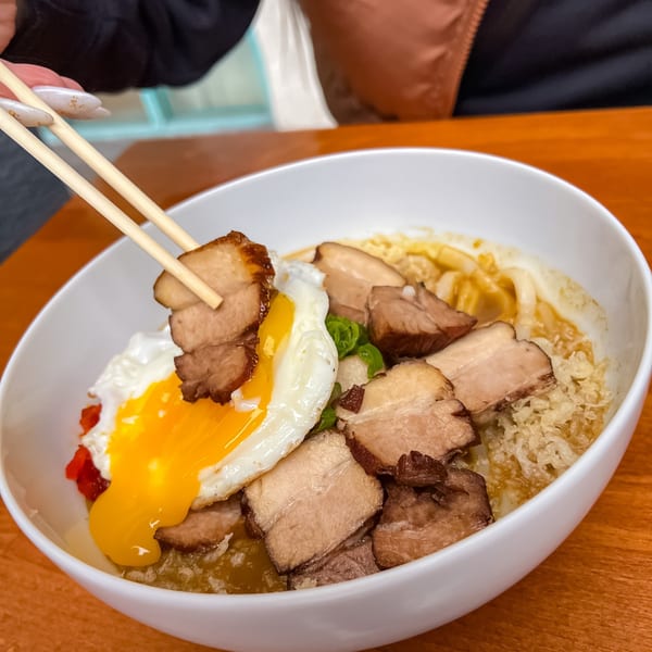 Chopsticks lifting a piece of chashu pork from a Japanese curry bowl with a fried egg.