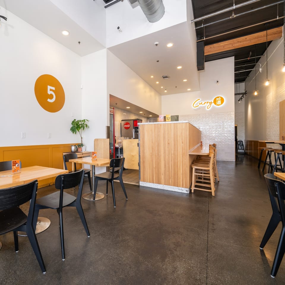 Interior of Curry Do, a Japanese restaurant, with tables, chairs, and a service counter.